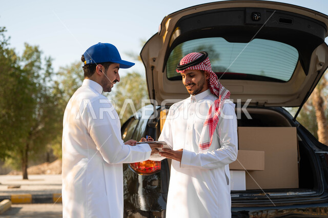 ايماءات الرضا والسعادة عند وصول الطرد، التوقيع على استلام الطلبية بشكل سليم، رجلان عربيان سعوديان خليجيان يرتديان الزي التقليدي ويقفان أمام سيارة شحن البضائع، جودة شركات الشحن السعودية