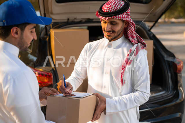 ايماءات الرضا والسعادة لوصول الطلبية بشكل سليم، جودة شركات الشحن والتوصيل، صورة مقربة لشاب عربي سعودي خليجي يرتدي الثوب والشماغ التقليدي يقوم بالتوقيع على استلام الطلب، طلبات الاونلاين الامنه