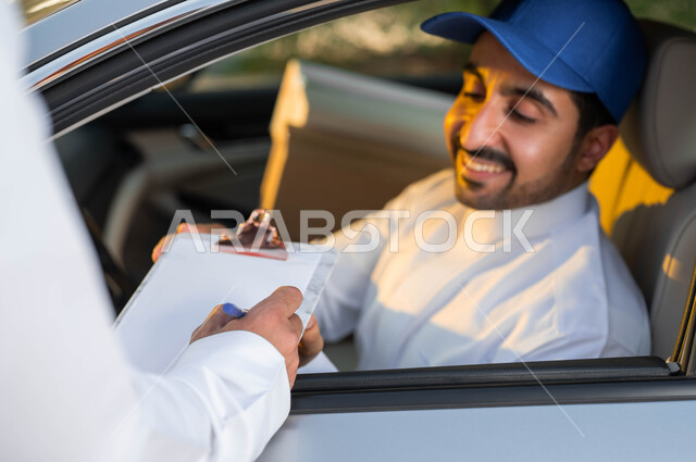 تسليم البضائع و الطلبات للزبائن، صورة مقربة لمندوب توصيل عربي خليجي سعودي مبتسم يرتدي قبعة زرقاء يجلس داخل السيارة بإيماءات البشاشة والرضا, التوقيع على أوراق و مستندات استلام و تسليم الطرد, خدمات التوصيل السريعة في السعودية.