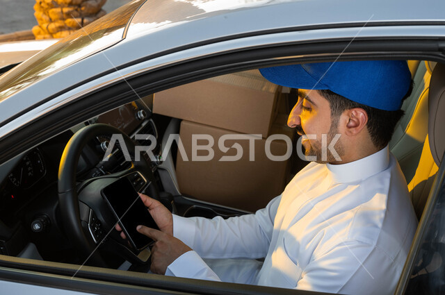 الاستعداد للانطلاق إلى العمل، صورة مقربة لمندوب توصيل عربي خليجي سعودي يرتدي الزي التقليدي والقبعة الزرقاء يحمل بيده الهاتف المحمول بشاشة سوداء فارغة، استخدام التقنيات الحديثة في تحديد الموقع، استعمال التكنولوجيا في الحياة العملية، مفهوم التسوق الالكتروني