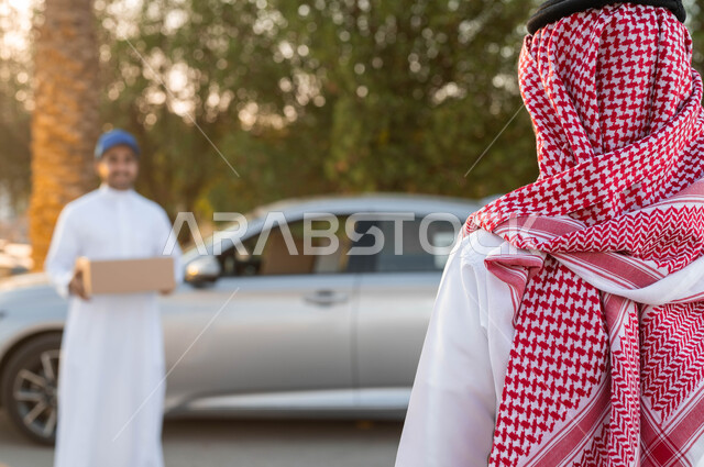 خدمة الديلفري السريعة والآمنة، مندوب توصيل عربي خليجي سعودي يرتدي الزي التقليدي يقوم بحمل طرد لتسليمه ، الثقة المتبادلة بين العميل وشركات الشحن، مفهوم التسوق الالكتروني، توصيل البضائع والطلبات للزبائن، الشراء عن طريق الانترنت