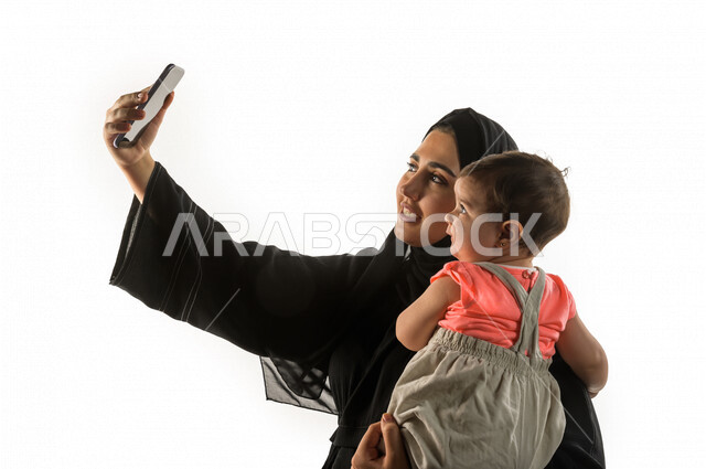 بورتريه لامرأه عربية سعودية خليجية مع ابنها الرضيع ،تلتقط صورة سلفي بهاتفها المحمول ، حياه الامومة ، الاهتمام و رعاية الأطفال ، التعامل مع الأطفال الرضع ، خلفية بيضاء