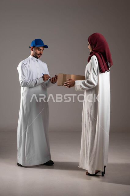 Online shopping and ordering feature, portrait of a Saudi Arabian Gulf woman wearing a white abaya and red hijab receiving a cardboard box, delivery representative writing down delivery information, fast and reliable shipping and delivery services, full length of the body, gray background