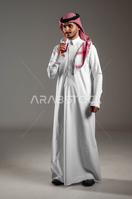 اعطاء شعور بالانتعاش وتحسين المزاج، بورتريه مقرب لرجل عربي خليجي سعودي يرتدي الملابس التقليديه والشماغ يستمتع بشرب العصير الطبيعي البارد، توفير العناصر الغذائية الضرورية للجسم، صوره لكامل الجسم، خلفيه ملونه