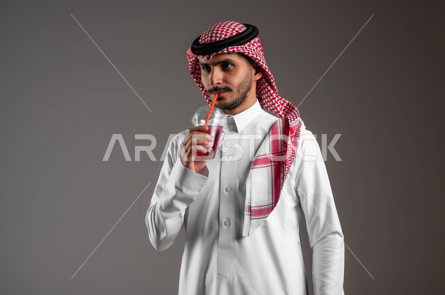 توفير العناصر الغذائية الضرورية للجسم، بورتريه مقرب لرجل عربي خليجي سعودي يرتدي الملابس التقليديه والشماغ يستمتع بشرب العصير الطبيعي البارد، تحسين المزاج واعطاء شعور بالانتعاش، الحفاظ على اللياقة البدنية، خلفيه رماديه