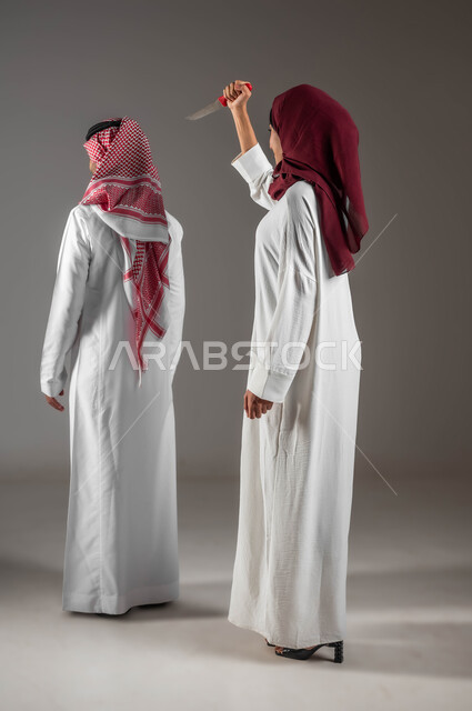 استخدام العنف في الزواح، سوء تفاهم ومشاكل عائلية ، بورتريه لامرأة عربية خليجية سعودية ترتدي عباءه بيضاء مع حجاب احمر تحمل بيدها سكين وتحاول قتل زوجها، الامراض النفسيه والمشاكل الزوجيه , العلاقات الاسريه الفاشلة، صورة الجسم بالطول الكامل، خلفية رمادية