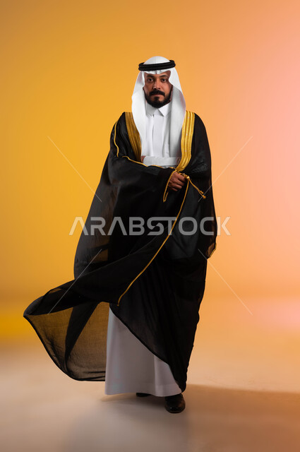 السرور والفرح في ليلة الزواج،  أناقة وفخامة اللباس الرسمي التقليدي  للمناسبات الخاصة والاحتفالات، بورتريه لرجل عربي خليجي سعودي يرتدي الغترة والبشت الاسود، النظر الى الكاميرا بتعابير السعادة والثقة بالنفس، صورة الجسم بالطول الكامل، خلفية ملونة