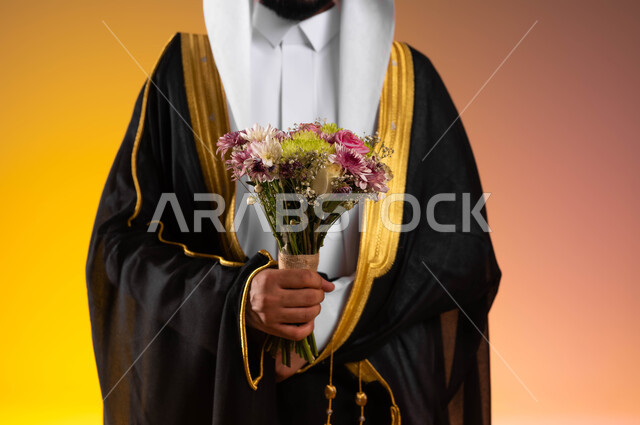 الاستعداد للتقدم وطلب الزواج، شراء الأزهار والورود الى العروس، بورتريه مقرب لعريس عربي خليجي سعودي يرتدي الغترة التقليدية والبشت الاسود يحمل بيده باقة ورد ملونة، مفهوم الاستقرار وتكوين عائلة سعيدة، مراسم الأعراس السعودية، خلفية ملونة