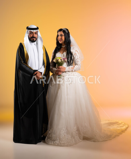 أصالة عادات وتقاليد مراسم الزواج في السعودية، بورتريه لعروس عربية خليجية سعودية تحمل باقة الورود تنظر الى زوجها بحب وسعادة، ارتداء العريس البشت الاسود والنظر الى الكاميرا بتعابير الثقة، مفهوم الزواج والاستقرار وتكوين عائلة، صورة لكامل الجسم، خلفية ملونة
