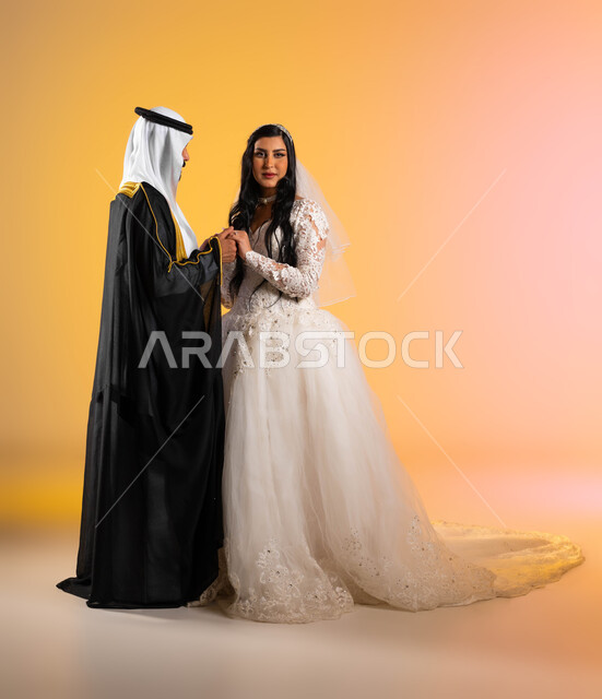 نظرات مليئة بالرومنسية والحب، مراسم الأعراس والحفلات في المملكة، مفهوم التزيين والاطلالة المتأنقة، بورتريه لعروس عربية خليجية سعودية مبتسمة ترتدي فستان الزفاف الأبيض تنظر الى زوجها بتعابير المودة, صورة الجسم بالكامل، خلفية ملونة