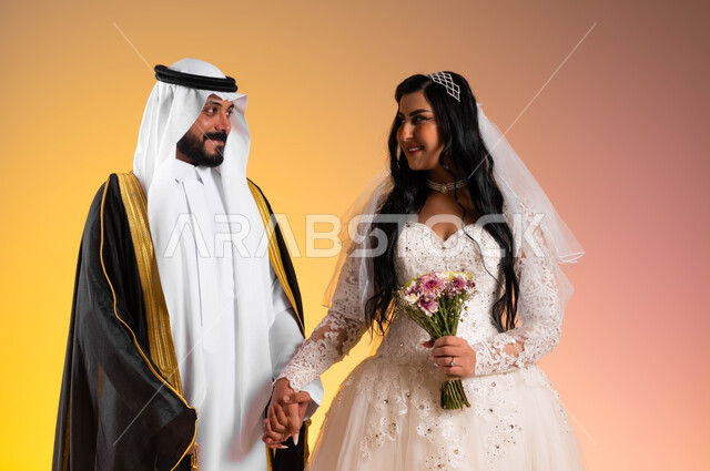 تعابير وايماءات السعادة والسرور في يوم الزواج، بورتريه مقرب لعروس عربية خليجية سعودية مبتسمة ترتدي فستان الزفاف الأبيض تحمل بيدها باقة ورد تقوم بتبادل نظرات الحب مع زوجها, مفهوم تكوين الأسرة وتحقيق الاستقرار العاطفي، فخامة الأعراس في المملكة، خلفية ملونة