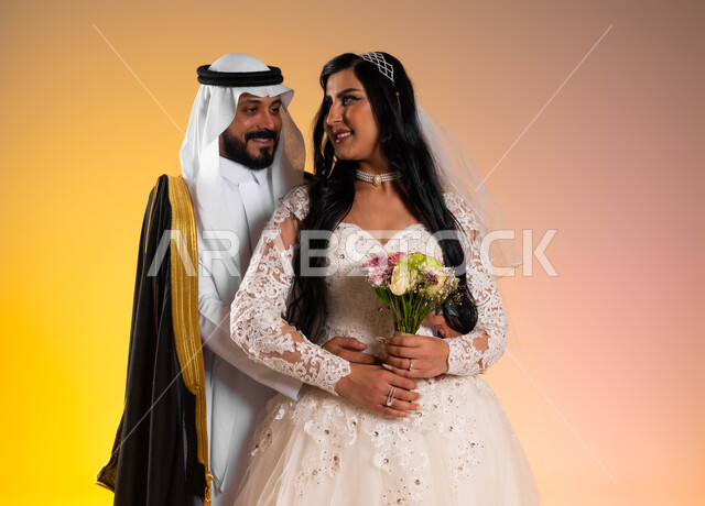 أصالة الأعراس في المملكة، مفهوم التزيين والاطلالة المتأنقة، بورتريه لعروس عربية خليجية سعودية مبتسمة ترتدي فستان الزفاف الأبيض تحمل بيدها باقة ورد، عريس ينظر الى زوجته بتعابير المودة, نظرات مليئة بالرومنسية والحب، خلفية ملونة