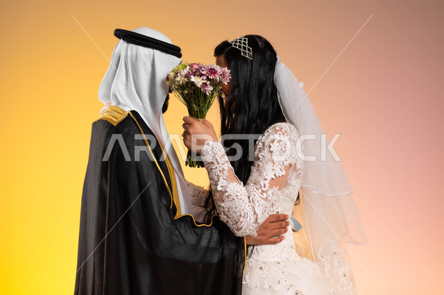 مفهوم الاستقرار وتكوين العائلة، الحياء والخجل عند النساء، بورتريه مقرب من الجانب لعريس عربي خليجي سعودي يرتدي البشت والغترة التقليدية يقف بجانب زوجته، عروس ترتدي فستان الزفاف وتغطي وجهها ووجه زوجها بباقة الورد، لحظات وأجواء رومنسية في يوم العرس, خلفية ملونة