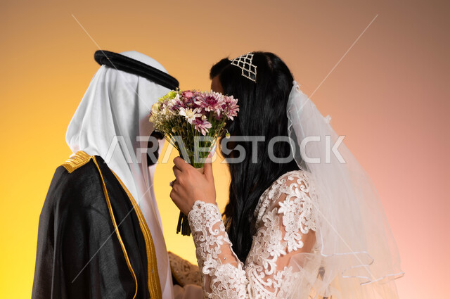 الحياء والخجل عند النساء، مفهوم الاستقرار وتكوين العائلة، بورتريه مقرب من الجانب لعريس عربي خليجي سعودي يرتدي البشت والغترة التقليدية يقف بجانب زوجته، عروس ترتدي فستان الزفاف وتغطي وجهها ووجه زوجها بباقة الورد، لحظات وأجواء رومنسية في يوم العرس, خلفية ملونة