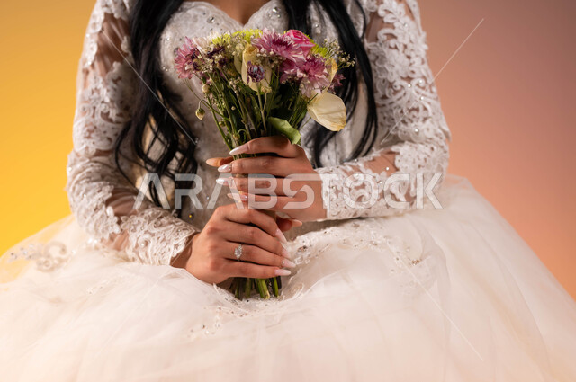 باقات أزهار مميزة وفريدة، بورتريه مقرب لعروس عربية خليجية سعودية ترتدي فستان الزفاف الأبيض تحمل بيدها باقة ورد، مفهوم التزين والاطلالة المتألقة في يوم العرس، مراسم الأعراس والزواج في السعودية، خلفية ملونة