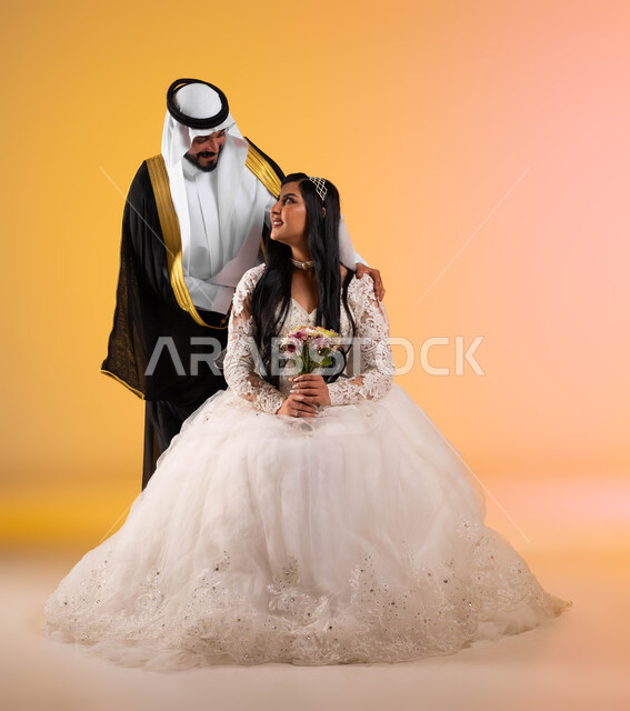 Wedding parties in the Kingdom, gestures of joy and happiness on the night of life, the concept of stability and forming a family, a portrait of a Saudi Gulf Arab groom wearing a bisht and ghutra, placing his hands on his wife’s shoulders, a bride wearing a white wedding dress holding a bouquet of flowers, full-length body, colored background