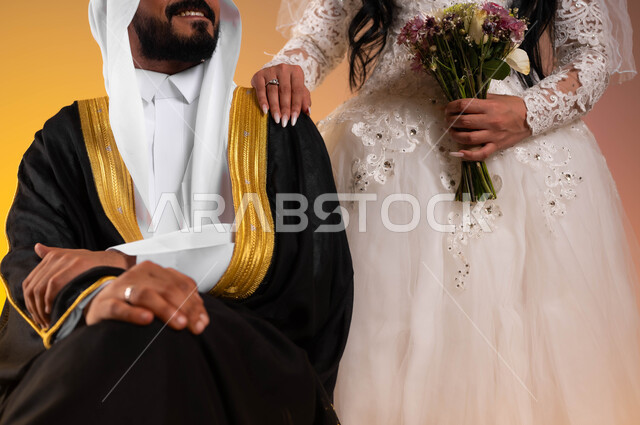 Love and affection between the newlyweds, gestures of joy and happiness on the wedding day, a close-up portrait of a smiling Saudi Arabian Gulf groom sitting and wearing the traditional bisht and ghutra, a Saudi bride wearing a white wedding dress placing her hand on her husband’s shoulder, wedding and marriage ceremonies in Saudi Arabia, a colorful background