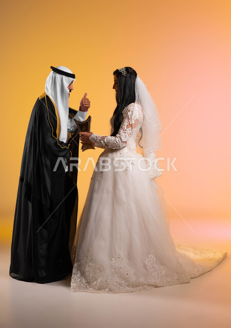 الاهتمام بالمظهر الخارجي، التطيب بالمسك والعود، مفهوم الاستقرار وتكوين عائلة، بورتريه من الجانب لعروس عربية خليجية سعودية تحمل بيدها المبخرة وتعطر زوجها، ارتداء الأزياء الخليجية الفاخرة، مراسم الأعراس والمناسبات في المملكة، الطول الكامل للجسم، خلفية ملونة