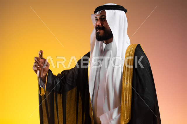 مراسم الأعراس والزواج في السعودية، عطور ذات روائح فاخرة، استخدام الزيوت العطرية الطبيعية، بورتريه مقرب لرجل عربي خليجي سعودي يرتدي البشت والغترة التقليدية يقوم برش العطر، مفهوم الأناقة والاهتمام بالمظهر الخارجي، خلفية ملونة