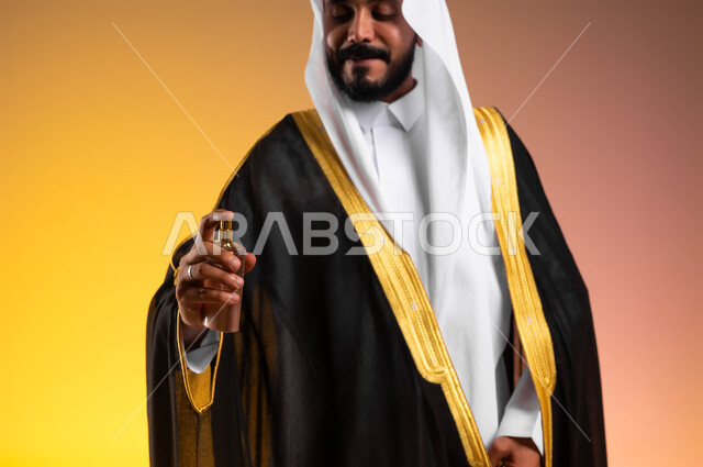 عطور ذات روائح فاخرة، استخدام الزيوت العطرية الطبيعية، بورتريه مقرب لرجل عربي خليجي سعودي يرتدي البشت والغترة التقليدية يقوم برش العطر، مفهوم الأناقة والاهتمام بالمظهر الخارجي، مراسم الأعراس والزواج في السعودية، خلفية ملونة