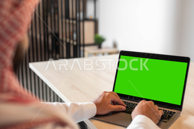 دور التكنولوجيا في في تسهيل الأعمال، استعمال الحاسوب المحمول في إنجاز العمل، تصفح الانترنت باستخدام الأجهزة الحديثة، صورة مقربة من الجانب لرجل عربي خليجي سعودي يرتدي الزي التقليدي والشماغ يقوم بالنقر على لابتوب بشاشة خضراء فارغة، كروما
