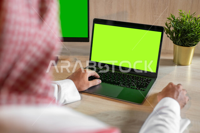 استخدام التكنولوجيا الحديثة والمتطورة للتعلم عن بعد، القيام بمقابلات وإجتماعات العمل أونلاين، صورة مقربة من الخلف لرجل عربي خليجي سعودي يقوم بمتابعة أخبار وسائل التواصل الإجتماعي، عرض شاشة خضرا فارغة على الأجهزة التقنية، كروما