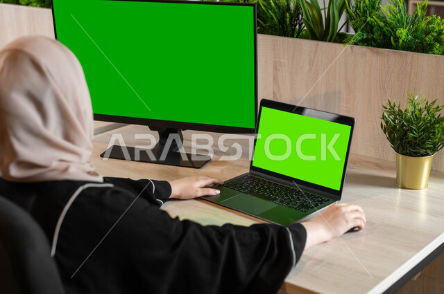 القيام بمقابلات وإجتماعات العمل عن بعد، مشاهدة الأفلام والمسلسلات عبر الإنترنت، أجهزة إلكترونية بشاشة خضراء فارغة، تصوير مقرب من الخلف لامرأة عربية خليجية سعودية تجلس خلف مكتب وتقوم بإنجاز المهام المطلوبة من خلال جهاز الحاسوب، كروما