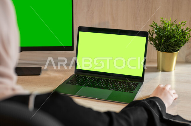 إجراء مقابلات وإجتماعات العمل عن بعد، مشاهدة الأفلام والمسلسلات عبر الإنترنت، أجهزة إلكترونية بشاشة خضراء فارغة، تصوير مقرب من الخلف لامرأة عربية خليجية سعودية تجلس خلف مكتب وتقوم بإنجاز المهام المطلوبة من خلال جهاز الحاسوب، كروما