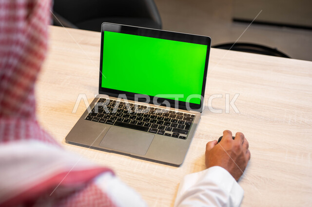 دور التكنولوجيا في العمل عن بعد, التواصل مع الاصدقاء بسهولة، عرض الأجهزة الالكترونية بشاشة خضراء فارغة، استعمال الحاسوب المحمول في إنجاز المهام، صورة مقربة من الخلف لرجل عربي خليجي سعودي يرتدي الثوب التقليدي يعمل على اللابتوب، كروما