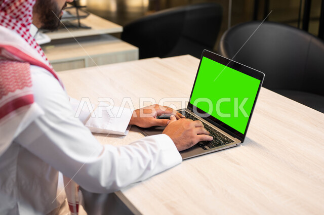متابعة مواقع التواصل الاجتماعي، عقد الاجتماعات عبر الانترنت، الدردشة و التواصل مع الاهل والأقارب، دمج التقنية والتكنولوجيا في الحياة العملية، صورة مقربة من الجانب لرجل عربي خليجي سعودي يرتدي الزي التقليدي يقوم بالنقر على اللابتوب بشاشة خضراء فارغة، كروما