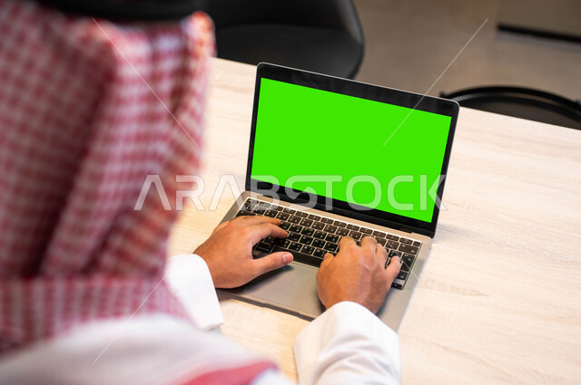 الدردشة و التواصل مع الاهل والأقارب، دمج التقنية والتكنولوجيا في الحياة العملية، متابعة مواقع التواصل الاجتماعي، عقد الاجتماعات عبر الانترنت، صورة مقربة من الخلف لرجل عربي خليجي سعودي يرتدي الزي التقليدي يقوم بالنقر على اللابتوب بشاشة خضراء فارغة، كروما