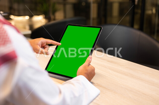 استخدام الأجهزة التقنية الحديثة لتصفح الصور والفيديوهات بسهولة، صورة مقربة من الخلف لرجل عربي خليجي سعودي يرتدي الزي التقليدي يحمل بيده جهاز التابلت بشاشه خضراء فارغة، القيام بمقابلات وإجتماعات العمل أونلاين، التواصل و الدردشة مع الاقارب, كروما