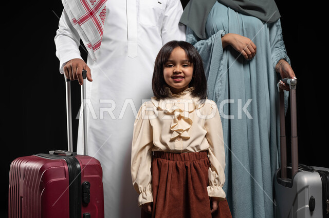 الاستعداد لقضاء إجازة صيفية والذهاب برحلة سياحية ممتعة مع الأهل، الحفاظ على الاستقرار والترابط الأسري، بورتريه مقرب لعائلة عربية خليجية سعودية يقفون بجانب حقائب السفر ويقومون بالنظر إلى الكاميرا، الأجواء العائلية السعيدة المليئة بالحب، خلفية سوداء