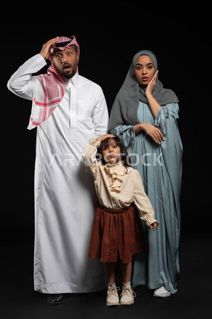 المفاجئة والدهشة لرؤية شيء ما، النظر الى الكاميرا بايماءات وحركات وجه ويدين تدل على الذعر والخوف، بورتريه لعائلة عربيه خليجية سعودية يرفعون أيديهم بتعابير الدهشة والذهول، صورة الجسم بالطول الكامل، خلفية سوداء
