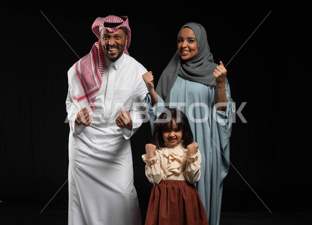 ايماءات الحماس والسعادة بالفوز الإنتصار والكسب، بورتريه لأسرة عربية خليجية سعودية يقومون برفع أيديهم للأعلى لتشجيع المنتخب المفضل، قضاء أوقات عائلية ممتعة مليئة بالحب، الحفاظ على الترابط الأسري والألفة والمودة بين الأفراد، خلفية سوداء