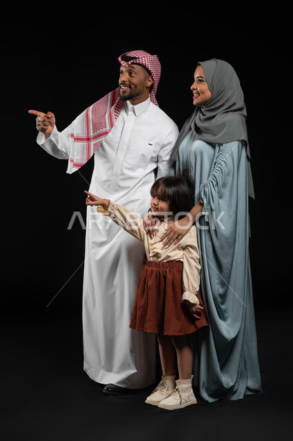 الأهداف والطموحات المستقبلية, مفهوم تربية الأبناء على الطريق الصحيح, بورتريه لعائلة عربية خليجية سعودية تقوم بالنظر والإشارة بإصبع السبابة بهدف لفت الإنتباه, ايماءات السعادة والسرور لرؤية شيء ما, أجواء عائلية مليئة بالحب, الطول الكامل للجسم, خلفية سوداء