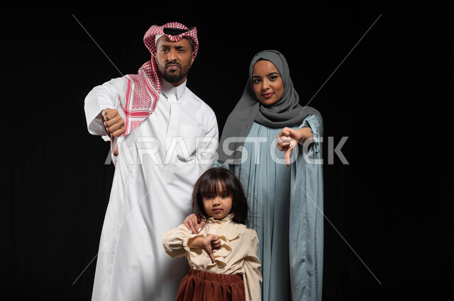 ايماءات وجه ويدين تدل على الرفض وعدم الموافقة, بورتريه لعائلة عربية خليجية سعودية تقف بإستقامة وتقوم بالنظر إلى الكاميرا, الإشارة بإصبع الإبهام الى الأسفل والإنزعاج من شيء ما, خلفية سوداء