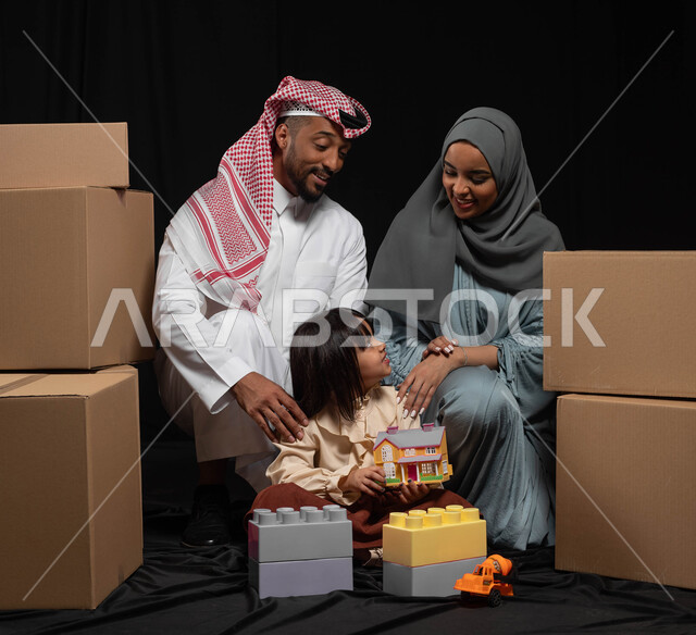 تعزيز الإبتكارات الذهنية والفكرية لدى الأبناء، قضاء وقت ممتع في اللعب مع الأهل، بورتريه لعائلة عربية خليجية سعودية تقوم بنشاط تركيب المكعبات مع بعضهم، رعاية وتشجيع مهارات الأولاد، الانتقال الى منزل جديد وترتيب صناديق الأغراض المنزلية، خلفية سوداء
