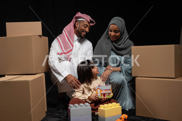 قضاء وقت ممتع في اللعب مع الأهل، تعزيز الإبتكارات الذهنية والفكرية لدى الأبناء، بورتريه لعائلة عربية خليجية سعودية تقوم بنشاط تركيب المكعبات مع بعضهم، رعاية وتشجيع مهارات الأولاد، الانتقال الى منزل جديد وترتيب صناديق الأغراض المنزلية، خلفية سوداء