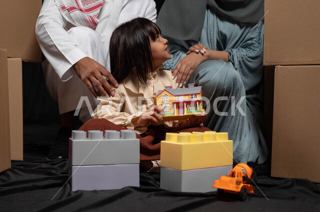 رعاية وتشجيع مهارات الأولاد، قضاء وقت ممتع في اللعب مع الأهل، تعزيز الإبتكارات الذهنية والفكرية لدى الأبناء، بورتريه مقرب لعائلة عربية خليجية سعودية تقوم بنشاط تركيب المكعبات مع بعضهم، الانتقال الى منزل جديد وترتيب صناديق الأغراض المنزلية، خلفية سوداء