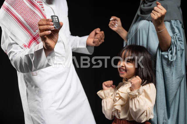مشاركة الأسرة فرحة تملك شيء جديد، بورتريه مقرب لرجل عربي خليجي سعودي يقف برفقة عائلته يحمل بيده مفتاح التحكم الالكتروني، ايماءات السعادة والسرور لإقتناء سيارة جديدة، الحفاظ على الاستقرار والأمان العائلي، خلفية سوداء