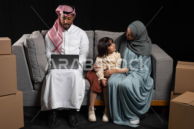 مفهوم الاستقرار العائلي، إجراء مكالمات فيديو أونلاين عن طريق الحاسوب المحمول، بورتريه لعائلة عربية خليجية سعودية تجلس في غرفة المعيشة، تبادل الاحاديث بين الام و الابنه، استخدام التقنيات الحديثة المتطورة, صناديق وحاويات كرتونية، خلفيه سوداء