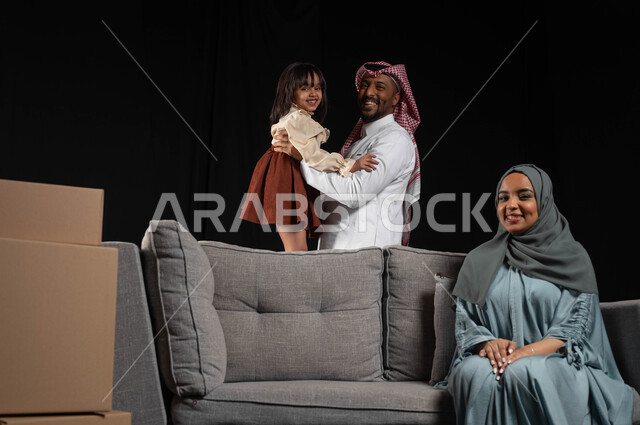 تدعيم أواصر المحبه والترابط الأسري، الانتقال الى منزل جديد, صناديق وحاويات كرتونية، بورتريه لسيده عربيه خليجيه سعوديه محجبة ترتدي العباءه الملونة تجلس على الاريكه الرماديه، بناء علاقة أسرية ناجحة وسعيدة، مسؤولية المرأة تجاه أولادها، خلفيه سوداء
