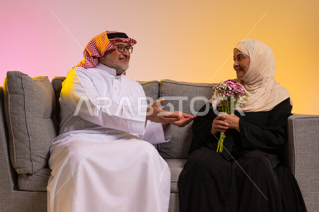 The concept of affection and compassion between spouses, the exchange of conversations between spouses, surprising the husband with flowers on holidays and occasions, gestures of tenderness and love, a portrait of an elderly Saudi Gulf Arab man extending his hands to his wife with love and appreciation, a colorful background.