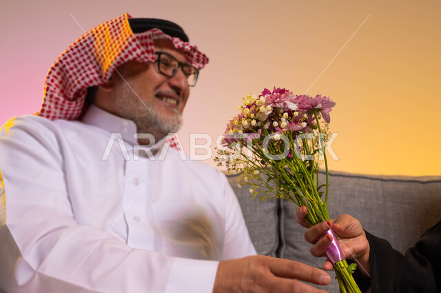 مفهوم احترام المرأة لزوجها وتقديره، الألفة والمودة بين الأفراد في الأسر السعودية، تعابير يد ووجه تدل على البهجة والسرور، الاحتفال بعيد الزواج، مفاجئة الزوج بالأزهار في الأعياد والمناسبات، بورتريه مقرب لرجل عربي خليجي سعودي يرتدي الزي التقليدي، خلفية ملونة
