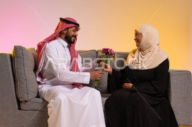 إسعاد الأم في الأعياد، التربية الصالحة للأبناء، تماسك وترابط الأسرة السعودية، مفهوم بر الوالدين والإحسان إليهما، إظهار الحب والاحترام والتقدير للأهل، بورتريه لأيدي شاب عربي خليجي سعودي يقوم بتقديم باقة من الأزهار لوالدته، خلفية ملونة