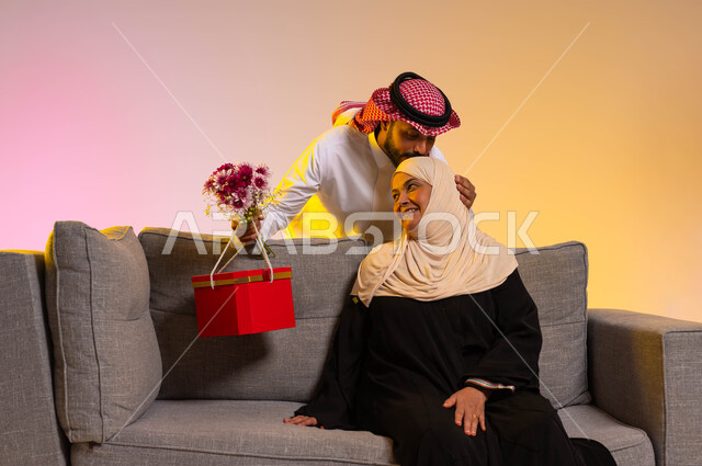 إيماءات الرضا والسعادة، إحياء ذكرى عيد الأم، مفهوم احترام وتقدير الوالدين ورد الجميل لهما، بورتريه لشاب عربي خليجي سعودي يقوم بتقبيل رأس والدته، تقديم الهدايا في الأعياد والمناسبات، إدخال السرور إلى قلب الأهل، تماسك الأسرة السعودية، خلفية ملونة