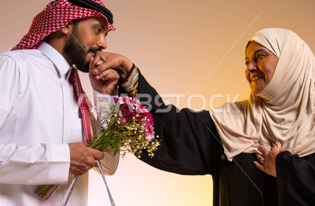 الاحترام والتقدير للوالدين ورد الجميل لهما، الترابط والتماسك الأسري، تقديم الهدايا والورود للأمهات في المناسبات والأعياد، بورتريه مقرب لشاب عربي خليجي سعودي يرتدي الزي التقليدي يقوم بتقبيل يد والدته، ايماءات البهجة والسرور، خلفية ملونة