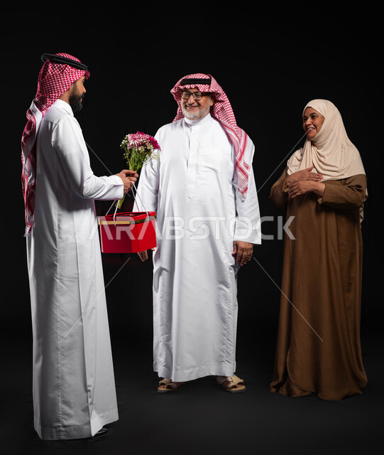 Family bonding and the exchange of affection and love between family members, surprising parents with gifts and presenting them with flowers, a happy family atmosphere, a portrait of a Saudi Arabian Gulf family wearing traditional dress celebrating holidays and occasions, full-body portrait, black background