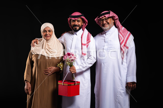 Family bonding and the exchange of affection and love between family members, a family atmosphere full of happiness, a portrait of a Saudi Gulf Arab family wearing traditional clothing looking at the camera with gestures of joy and pleasure, presenting gifts and flowers to the family on holidays and occasions, a black background